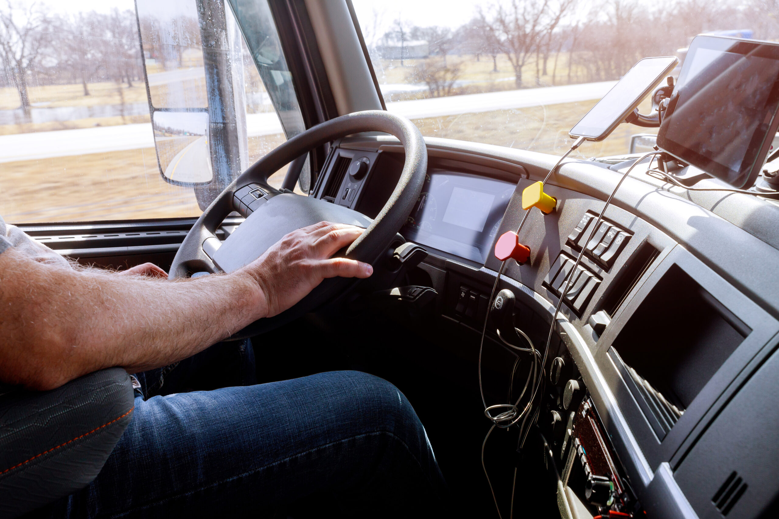 A truck driver operates a commercial semi-truck, with hands on the wheel and GPS devices on the dashboard